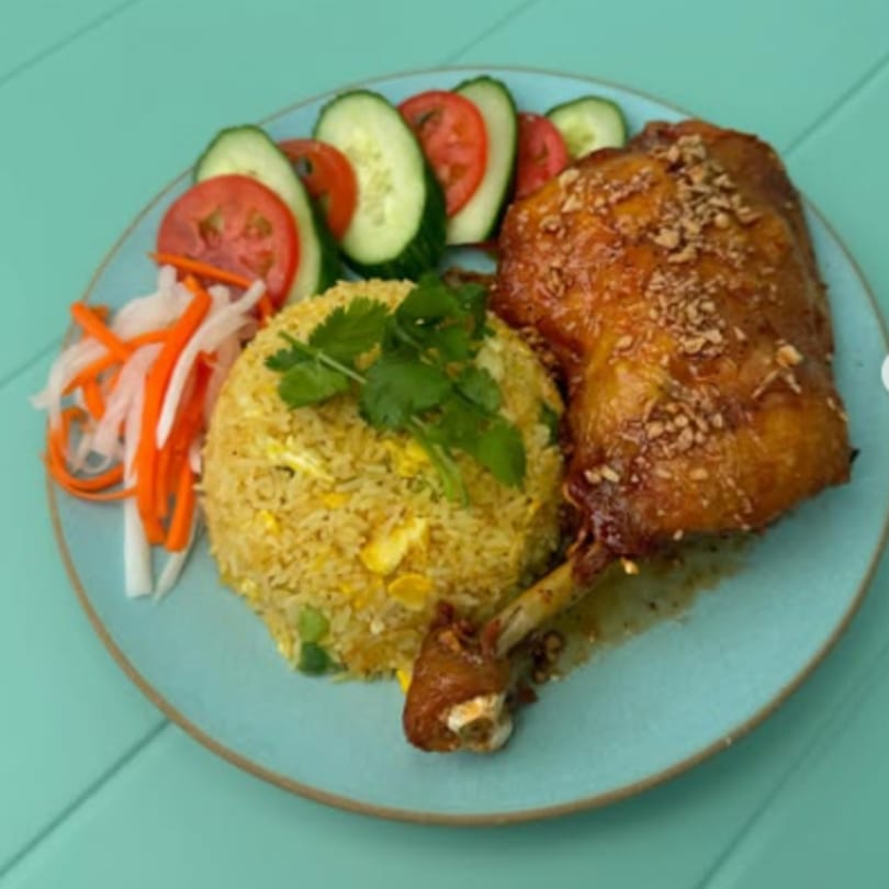 Vietnamese fried rice with a crispy chicken leg, pickled vegetables, and sliced cucumbers and tomatoes.