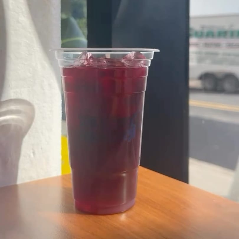 A plastic cup of iced hibiscus tea sits on a wooden table by a window at Jersey Banh Mi.
