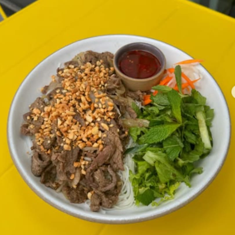 Vietnamese vermicelli noodle bowl with beef, peanuts, fresh herbs, and a side of sauce.