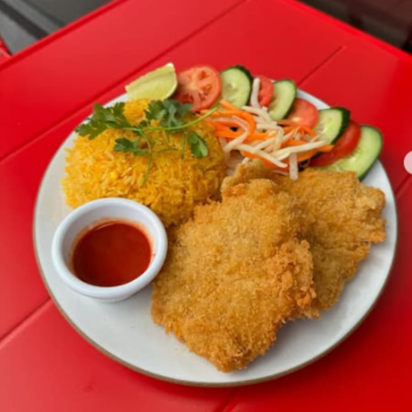 Crispy fried chicken cutlets with yellow rice, a side salad, and red dipping sauce on a white plate.