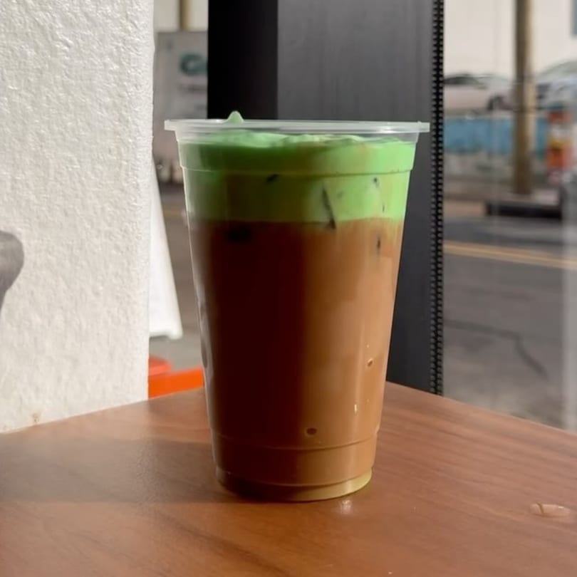 Iced coffee with a vibrant green foam topping in a clear plastic cup on a wooden table.