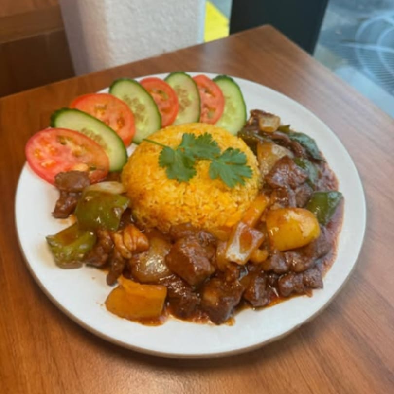 Vietnamese shaken beef with yellow rice, garnished with cilantro, sliced cucumbers, and tomatoes.