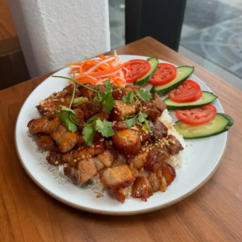 Vietnamese caramelized pork belly with rice, garnished with cilantro, pickled carrots, cucumbers, and tomatoes.